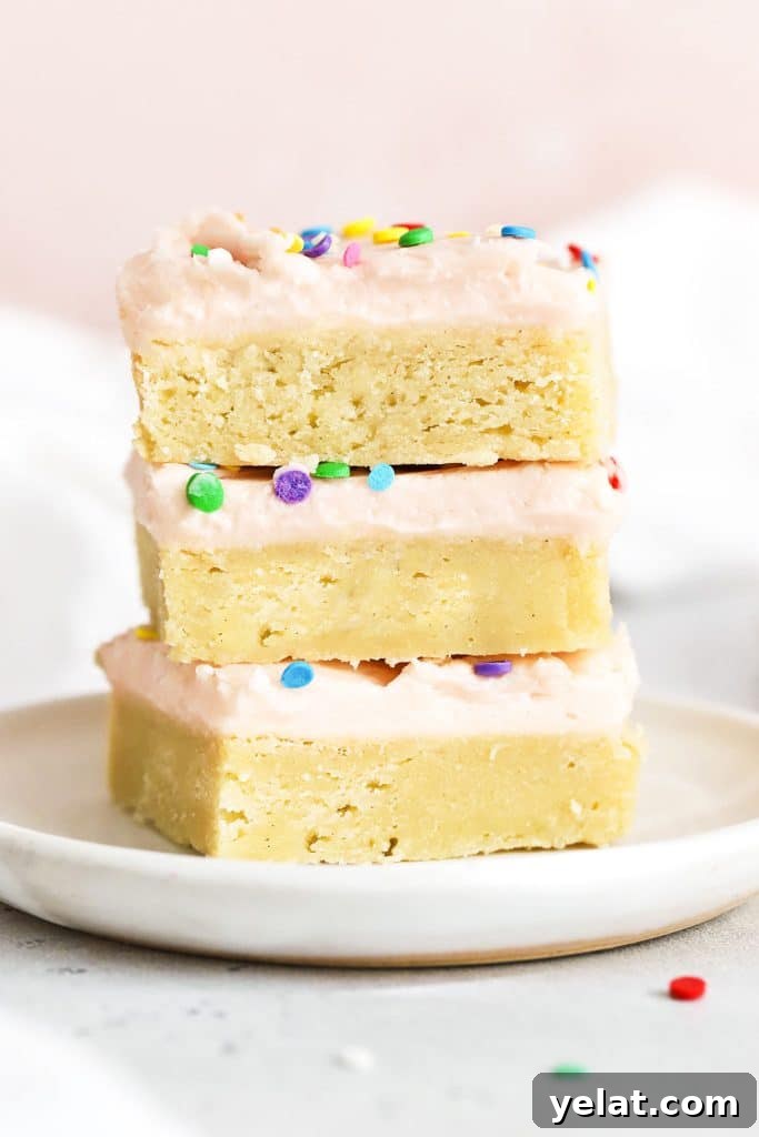 three sugar cookie bars with pink frosting stacked on a white plate