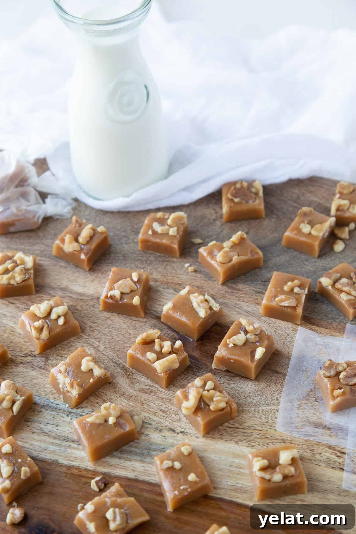 walnut caramels on a wooden board with a glass jug of milk nearby.