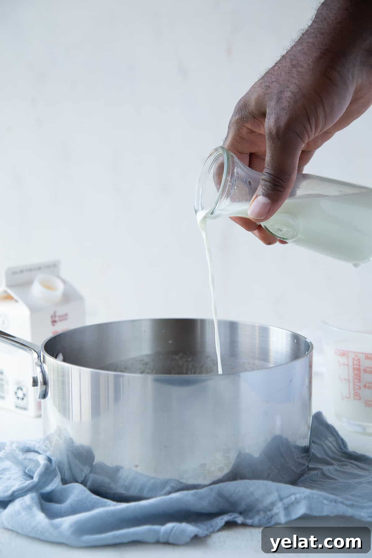 hand pouring heavy cream into a saucepan sitting on a blue tea towel.