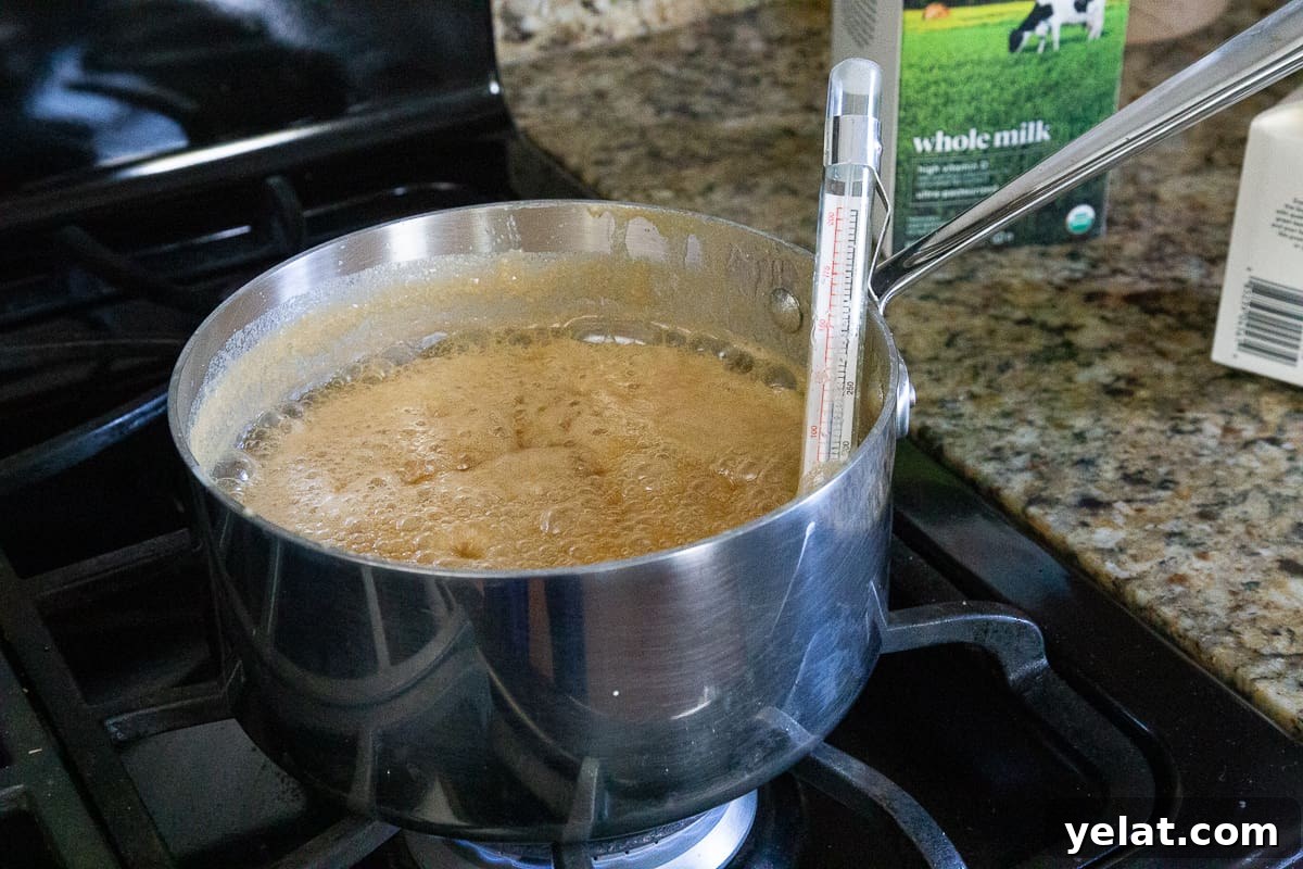 pot of caramel bubbling on the stove with a candy thermometer in the pot.