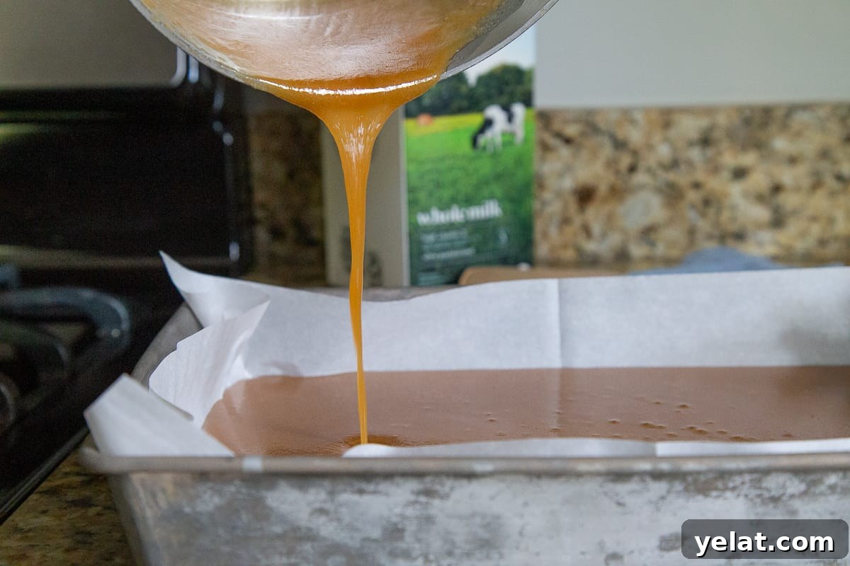 hand pouring caramel into a metal pan lined with parchment paper.