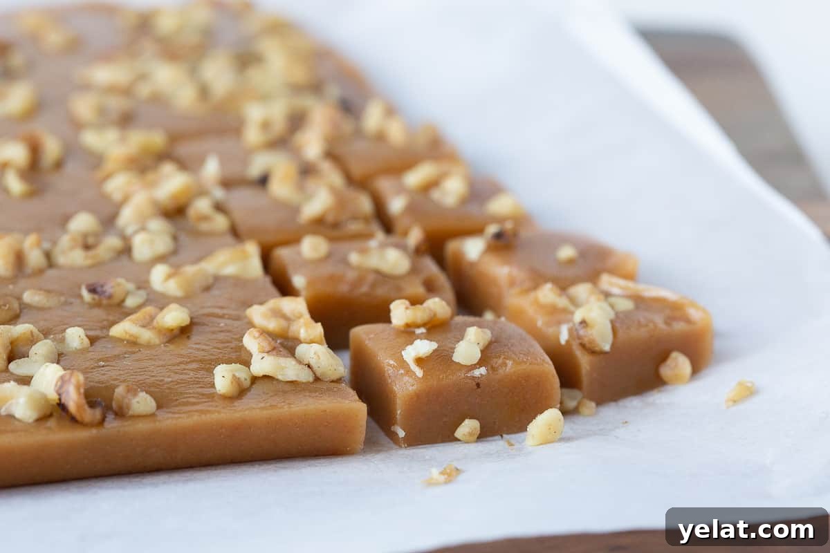 squares of caramels cut from a slab of caramels, topped with walnuts and sitting on parchment paper.