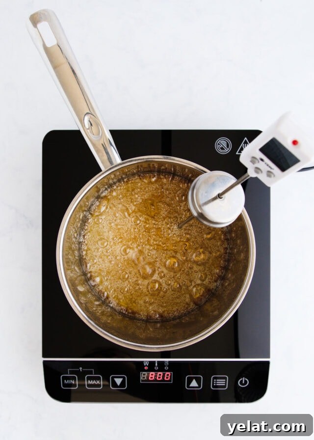 Homemade Rum Caramel Sauce Recipe for Desserts and Drizzling 7 The caramel beginning to turn golden, with a sugar thermometer clipped to the side of the pan.