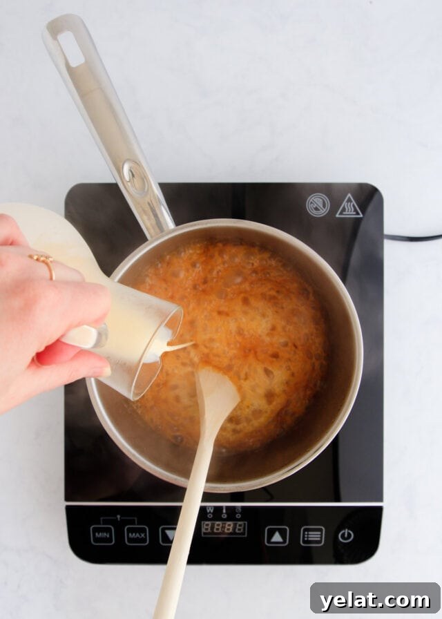 Homemade Rum Caramel Sauce Recipe for Desserts and Drizzling 9 The cream being poured into the caramel from a small glass jug.