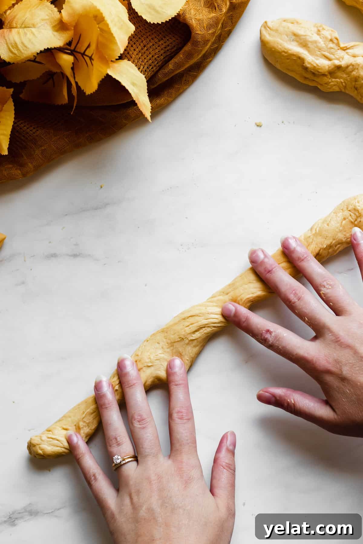 Two hands roll a piece of pumpkin pretzel dough