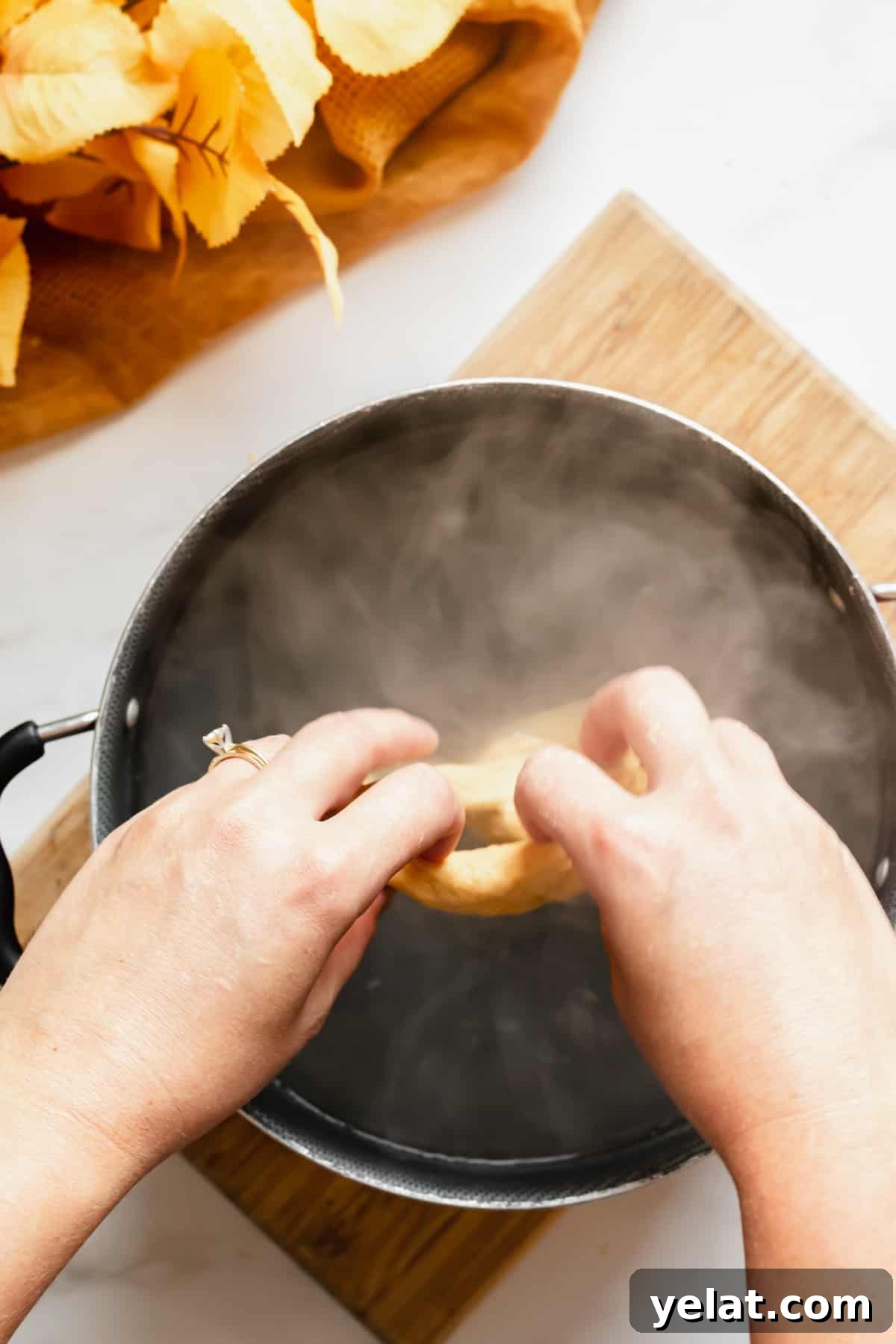 Two hands place a pretzel into a baking soda water bath