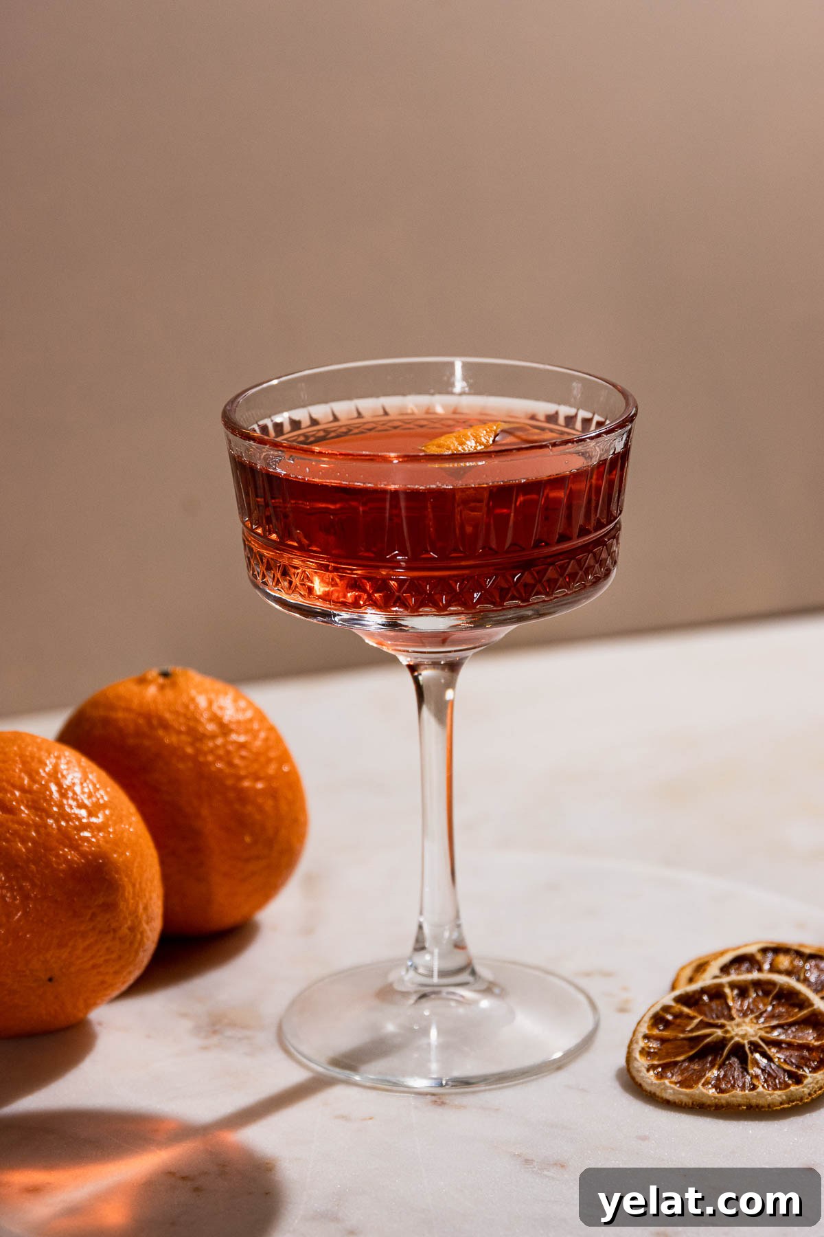 Side shot of a beautiful coupe glass filled with a dark orange cocktail. 
