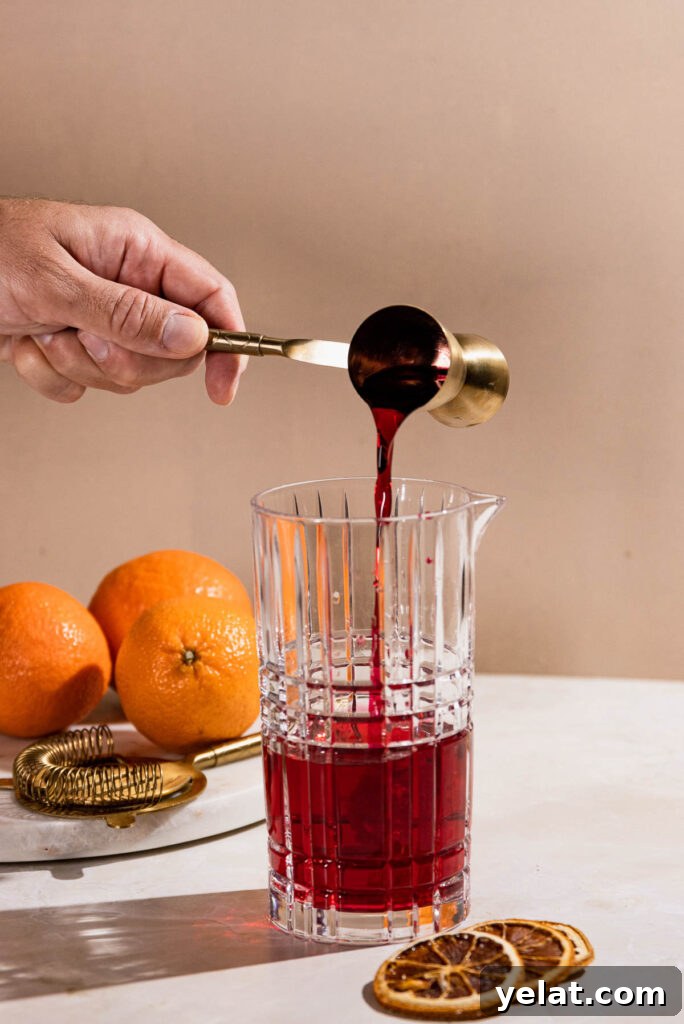 Grenadine poured from a jigger into a cocktail shaker. 