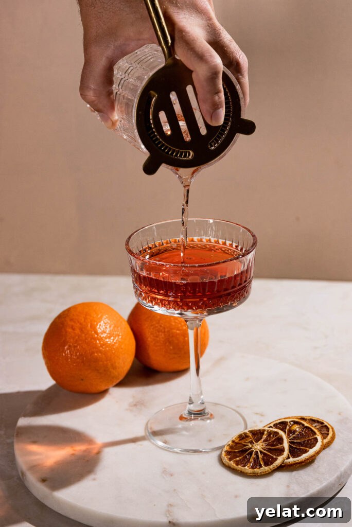 Hand straining cocktail into coupe cocktail glass. 