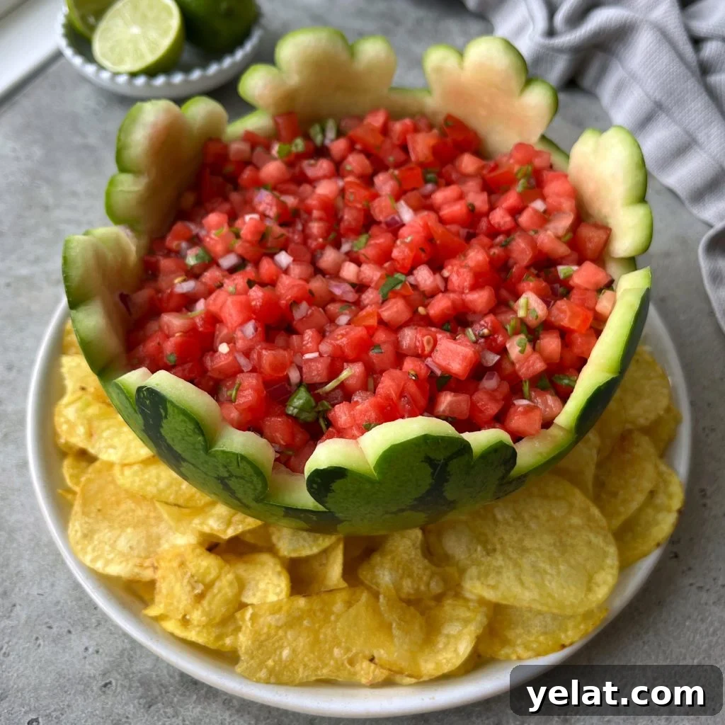 Fresh Watermelon Salsa Recipe for Summer Parties 2 A hollowed-out watermelon bowl filled with fresh watermelon salsa sits on a white plate surrounded by yellow tortilla chips. Lime wedges and a gray cloth are nearby.