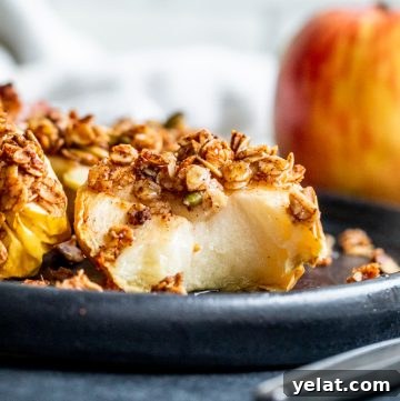 Crispy Air Fryer Apples with Honey Oat Crumble 13 Air fryer apple on a black plate with a bite out of it.