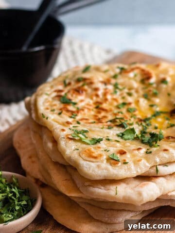 stack of sourdough naan on a wood board with cilatro and cast iron butter melter.