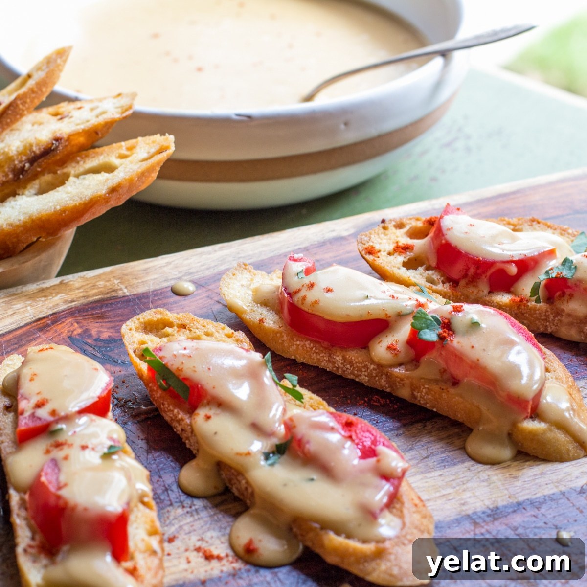 A serving board with crostini stacked with tomatoes, and drizzled with Welsh rarebit cheese sauce.