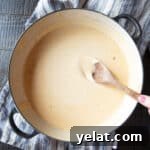 A wide-mouthed pan of Stouffer's Welsh Rarebit cheese sauce with a wooden spoon.